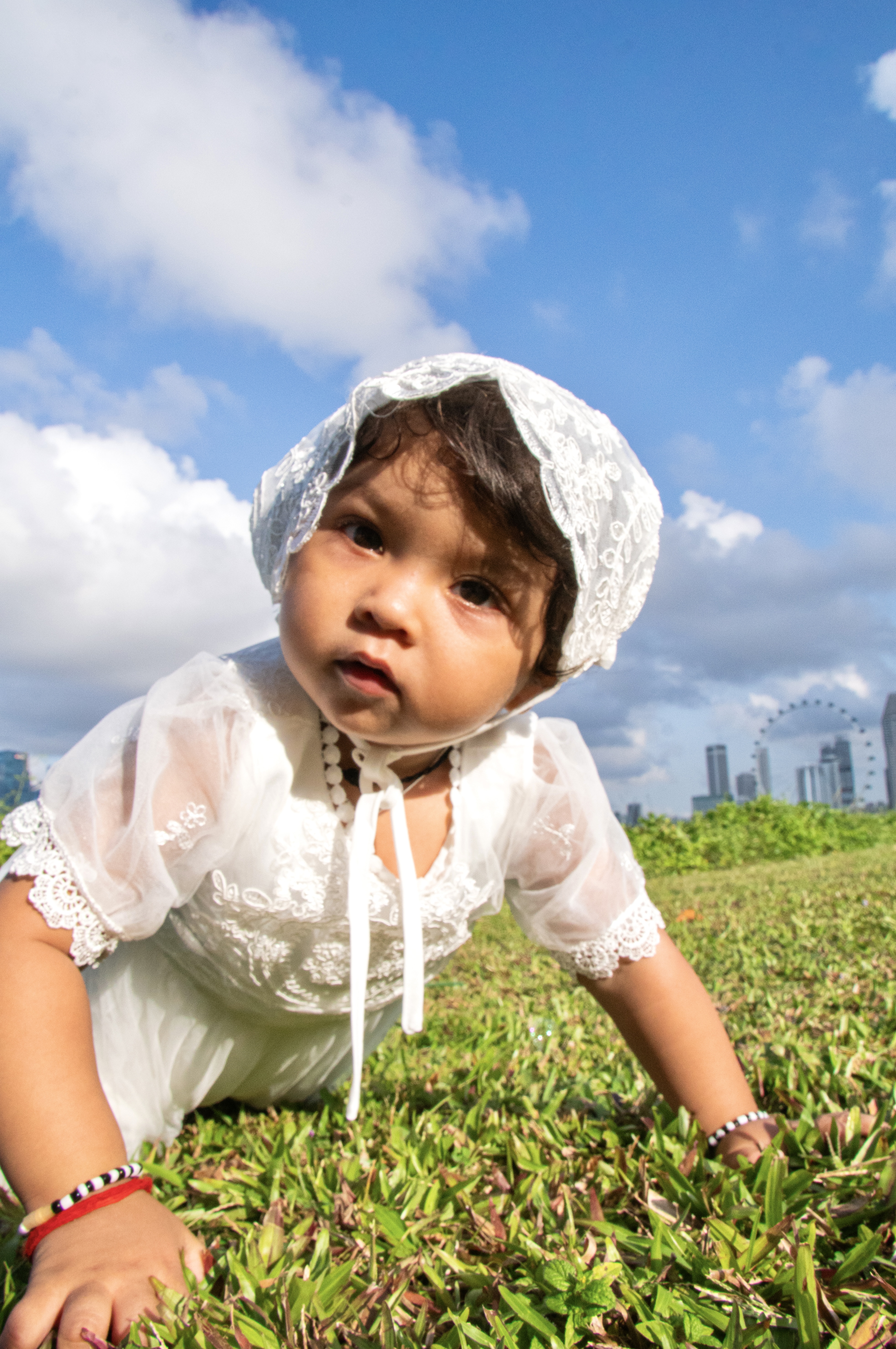 Baby in white dress crawling on grass with Singapore Flyer