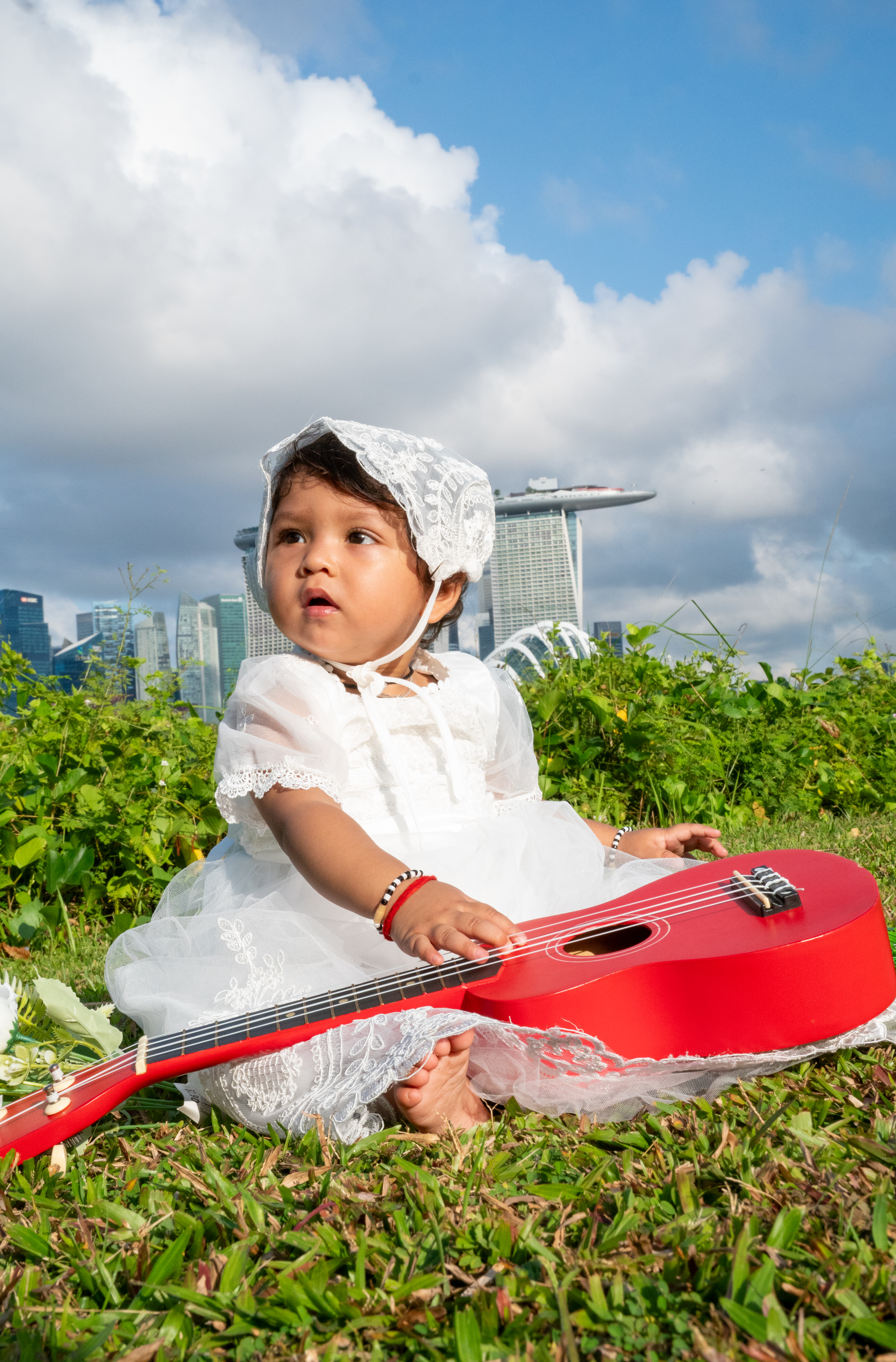 Baby in white dress with red guitar outdoors