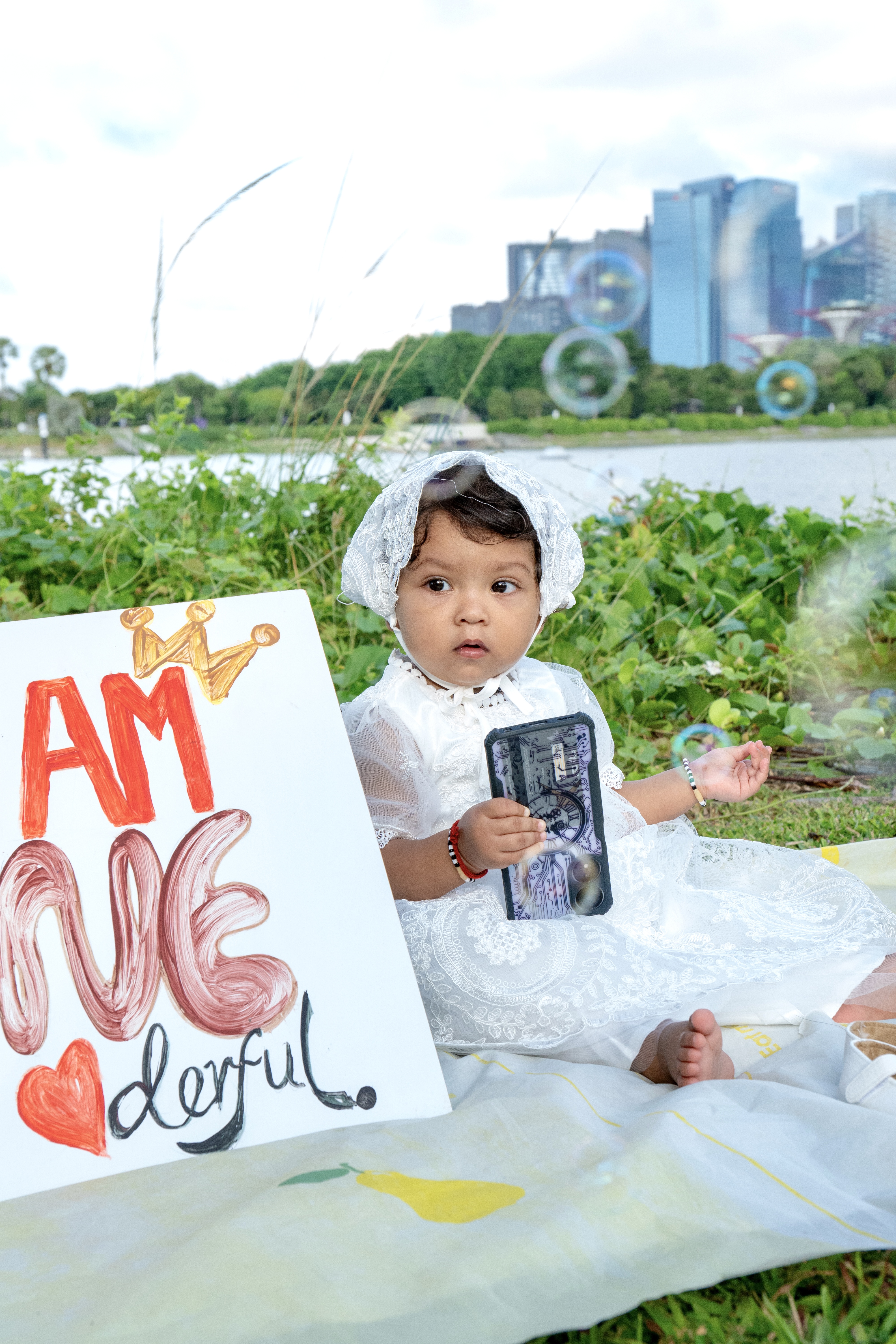Baby in white dress with sign outdoors